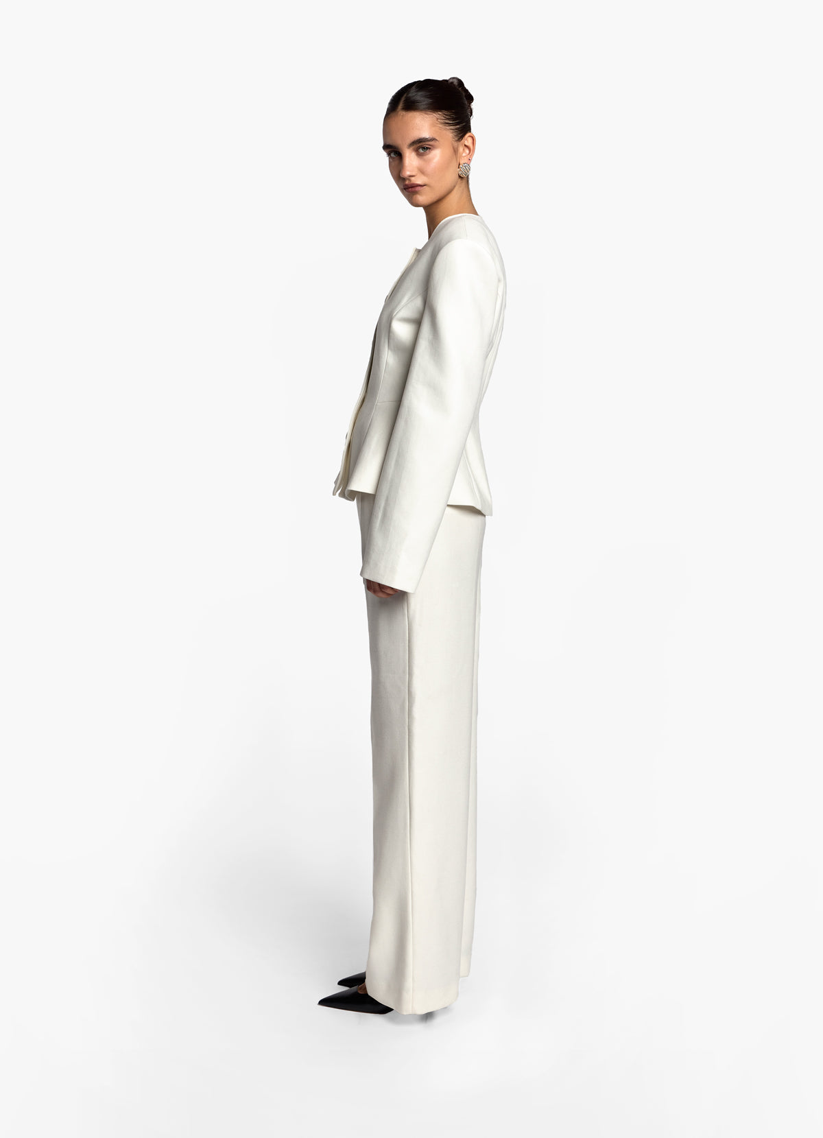 Side profile of model wearing cream wool fitted jacket and matching trousers.