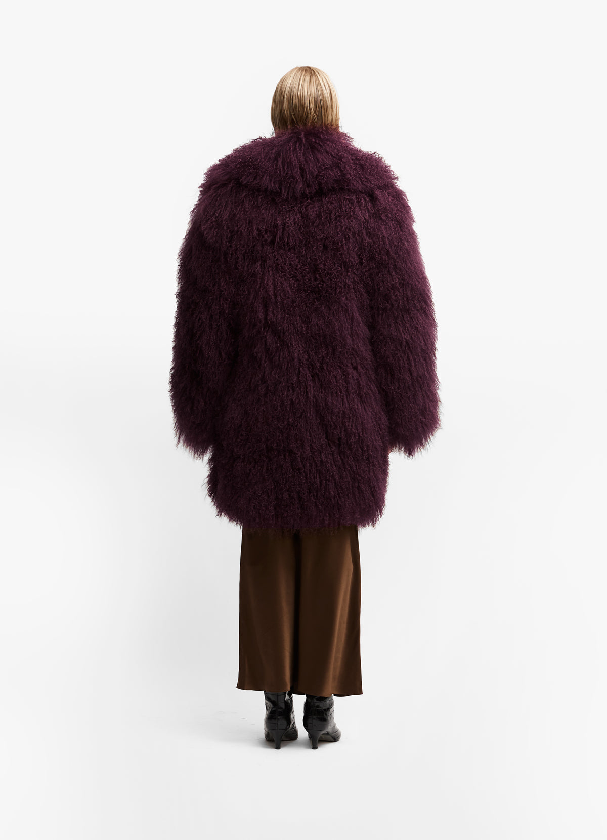Back shot of model wearing burgundy long length mongolian coat against white background.