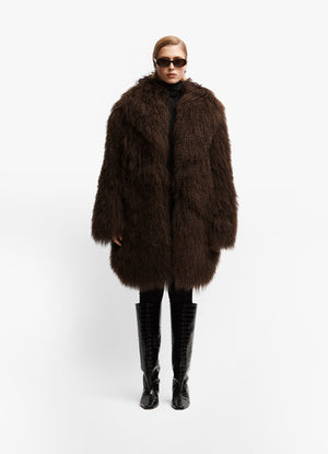 Model front facing wearing long brown mongolian wool coat with collar against white background.