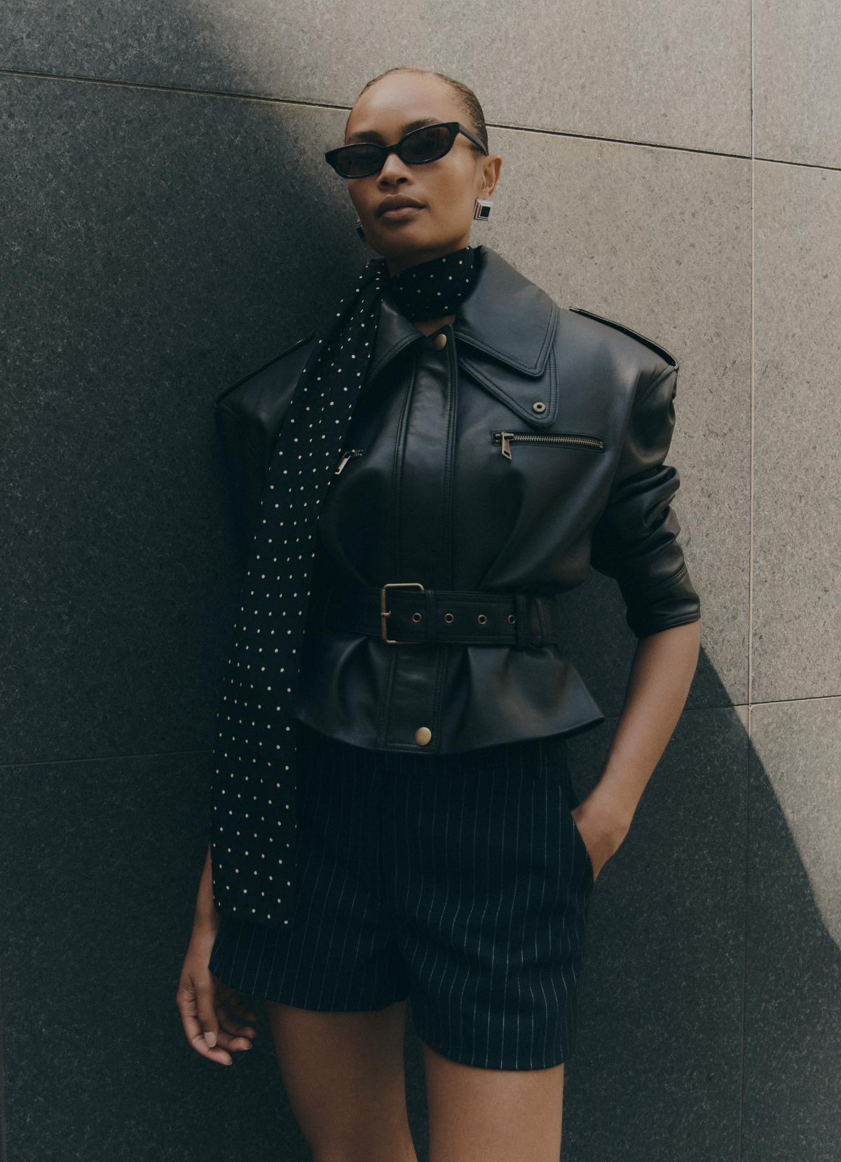 Close up of model wearing black leather cropped jacket with structured shoulders and biker detailing.