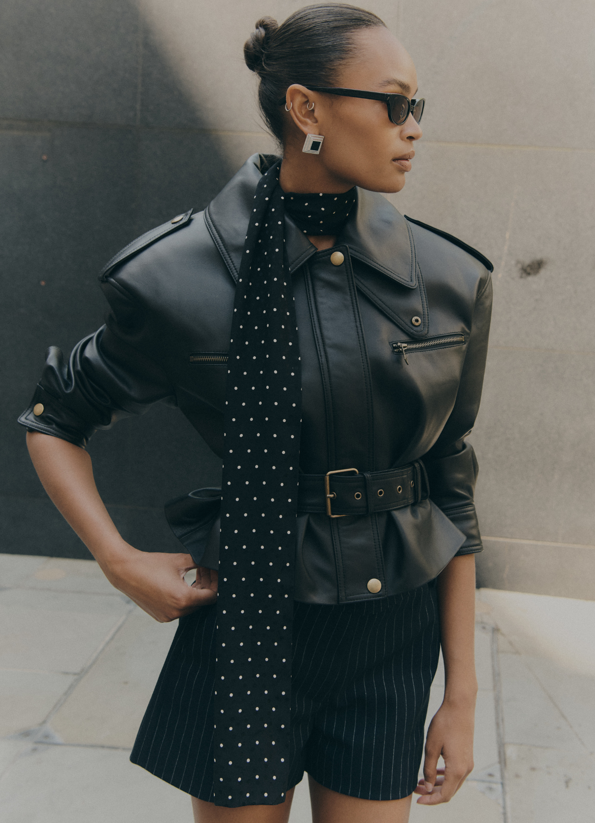 Detail shot of model wearing de Savary London black leather cropped jacket, jacket is fastened up with zip and waist belt.