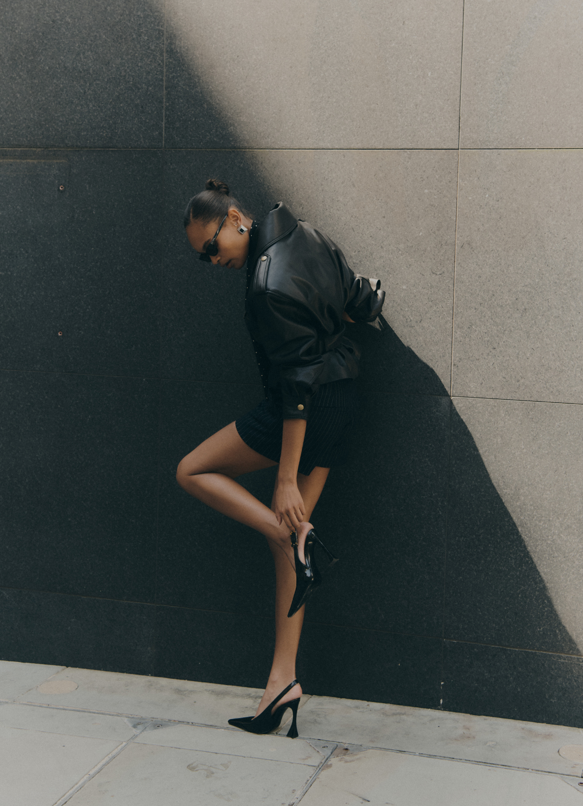 Image of model fixing shoe whilst wearing black cropped leather jacket from behind.